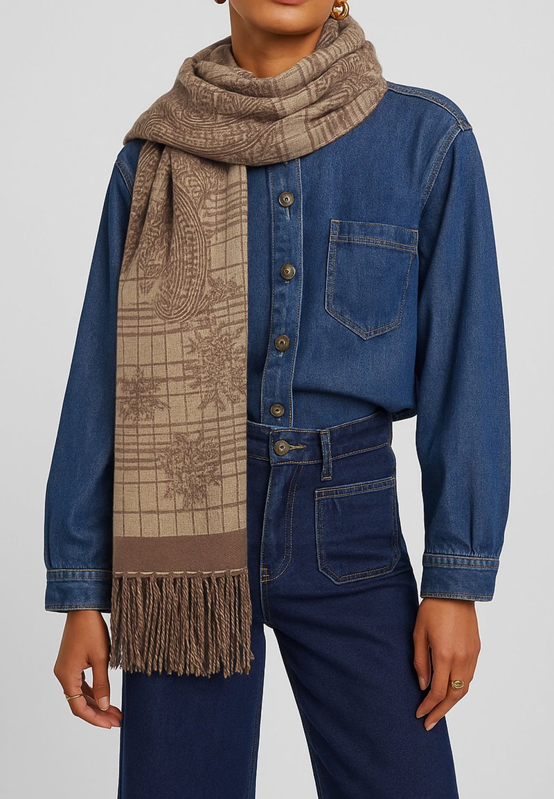 Sciarpa beige con un motivo a griglia testurizzato e bordi frangiati, posata su una camicia di denim con dettagli sui bottoni e una vestibilità classica.