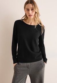 Maglietta nera a maniche lunghe con scollo rotondo e una texture morbida, abbinata a pantaloni elasticizzati grigi con tasche laterali.