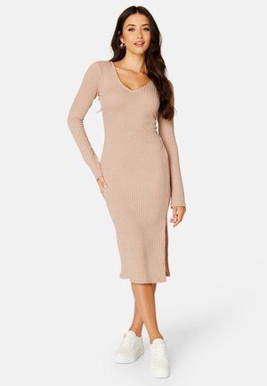 Strick-Midikleid in hellem Beige mit geripptem Muster, V-Ausschnitt, langen Ärmeln und seitlichem Schlitz, kombiniert mit weißen Sneakers.