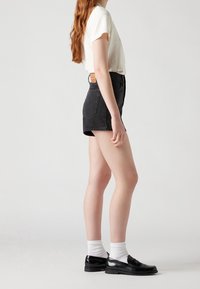 Svarta jeansshorts med hög midja, med fram- och bakfickor, i kombination med en krämfärgad t-shirt med kort ärm och svarta skor med vita strumpor.