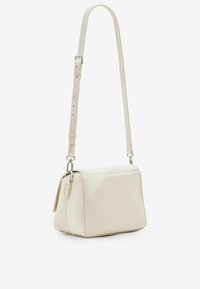 Beige Umhängetasche mit strukturierter Form, glatter Textur, verstellbarem Schulterriemen und silbernem Zubehör. Verfügt über schräge Nahtdetails.