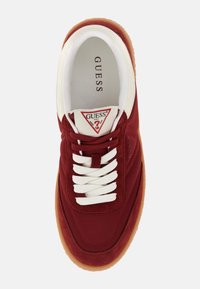 Red fabric sneaker with white laces and a rubber sole. Features a triangular logo label in red on the tongue. Smooth and textured materials.