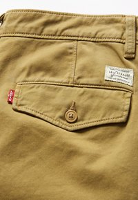 Poche arrière d’un pantalon Levi's beige avec fermeture à bouton, étiquette rouge Levi's et étiquette en tissu blanche siglée Levi Strauss.