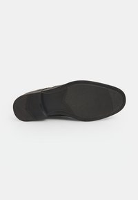 Črna čevljična podplat z teksturirano gumijasto oblogo. Ima zaobljeno obliko in izstopajoče vzorce. Gladek zgornji rob in neopazna peta.