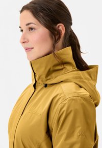 Yellow weatherproof jacket with a high collar and hood. Features textured fabric and logo detail on the chest and sleeve.
