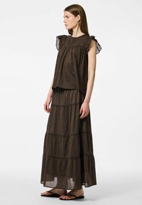 Top senza maniche marrone con maniche arricciate, abbinato a una lunga gonna coordinata con strati a balze e cuciture decorative.