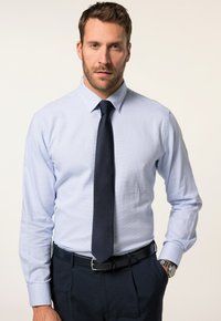 Camisa de vestir azul claro con mangas largas, cuello puntiagudo, tela texturizada, combinada con una corbata azul marino oscura y pantalones oscuros. Reloj plateado visible.