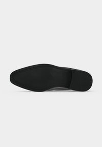 Semelle noire d'une chaussure habillée pour homme avec bout pointu et talon bas, présentée sur un fond gris clair.