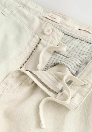 Shorts en lin beige clair avec fermeture éclair et bouton, dotés d'une doublure intérieure rayée et d'un cordon de serrage, présentant un tissu doux et texturé.
