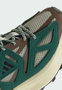 Scarpa sportiva verde e marrone con tessuto a rete, dettagli in camoscio e lacci a fantasia. Ammortizzazione Lightstrike visibile sulla suola.