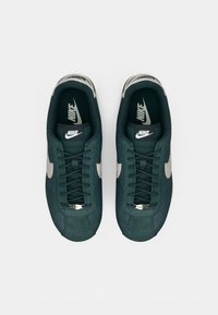 Nike tenisice s tamnozelenom nubuk gornjom, bež kožnim swooshom, crnim vezicama i podstavljenim jezikom s logotipom. Jednostavan, elegantan dizajn.