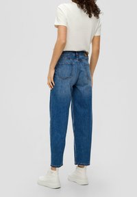 Light blue, high-waisted jeans with a relaxed fit, featuring two back pockets and hemmed cuffs, paired with a white short-sleeve shirt.