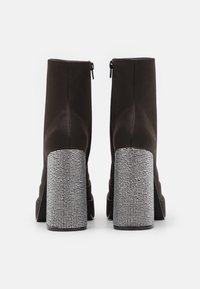 Par de botas de tobillo marrón oscuro con tacones altos y gruesos cubiertos de pequeñas piedras brillantes plateadas, vistas desde atrás.