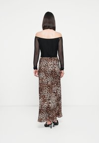 Haut noir dégageant les épaules avec de longues manches transparentes, associé à une jupe longue au motif léopard, avec de grandes taches brunes et noires. Chaussures noires.