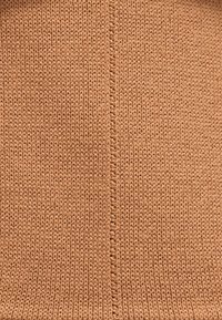 Nahaufnahme eines braunen Strickstoffs mit einer sichtbaren mittigen Naht, die senkrecht durch die Textur verläuft.