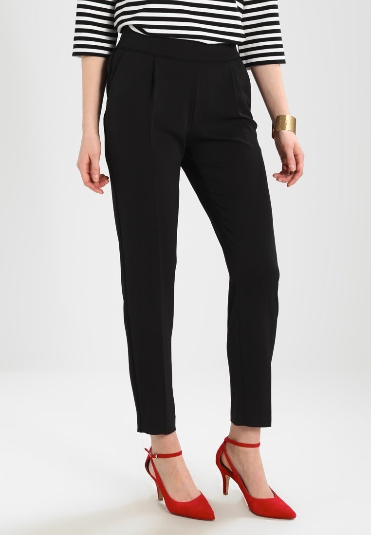 Woman wearing black slim-fit trousers, black and white striped top, gold cuff bracelet, and red high-heeled ankle strap shoes.