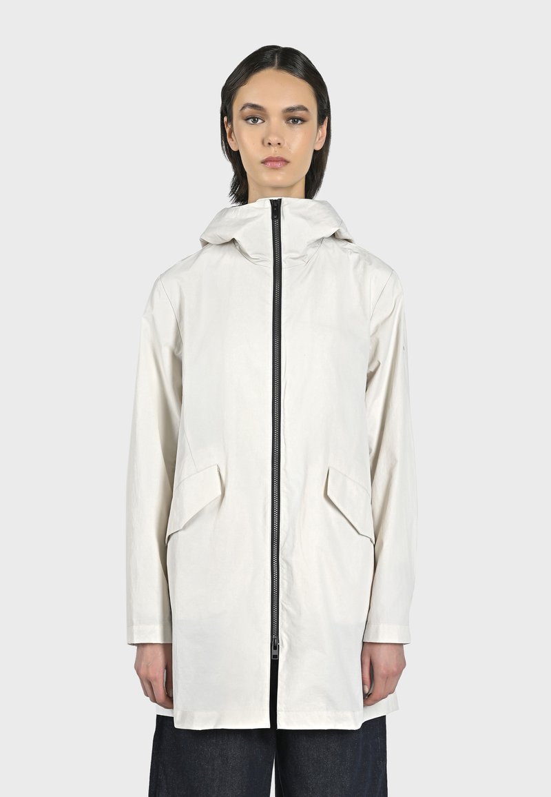 Giacca leggera di colore crema con cappuccio, caratterizzata da una chiusura centrale con zip, due tasche frontali a patta e una vestibilità rilassata.