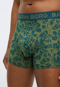 Πράσινα μποξερ με λουλουδάτο σχέδιο και μπλε ζώνη μέσης. Κατασκευασμένα από μαλακό ύφασμα με διακριτικές ραφές και εφαρμοστή γραμμή.