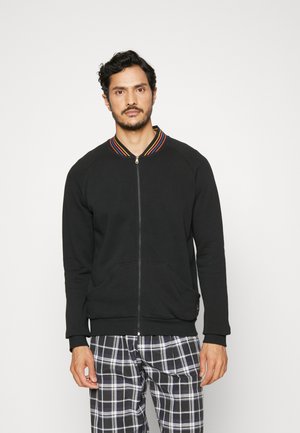 Sweat-shirt zippé noir avec un col côtelé multicolore à rayures, doté de deux poches avant et d'une coupe décontractée, associé à un pantalon à carreaux.