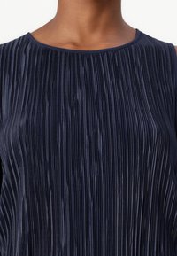 Navy pleated sleeveless top with a smooth texture and round neckline, featuring vertical lines and a sleek, flowing design.