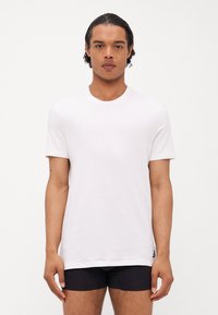 T-shirt blanc à manches courtes avec un col rond, fabriqué en coton doux, avec un logo de marque subtil sur l'ourlet gauche.