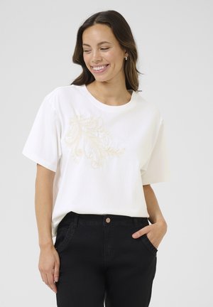 Vit t-shirt med korta ärmar, med blommig beige broderi framtill. Kombinerad med svarta byxor som har en avslappnad passform.