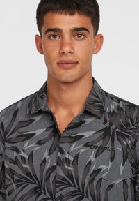 Button-up shirt with a dark gray background and black palm leaf pattern, featuring a collar and logo detail on the chest.