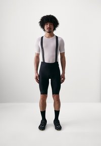 Shorts de cyclisme noirs avec bretelles, assortis à un t-shirt à manches courtes en mesh blanc. Caractéristiques d'un matériau élastique et d'un design ajusté.