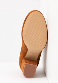 Tan suede-nahka blokki-korkokenkä, jossa on kuvioitu kumipohja ja ALDO-brändi, aseteltuna pohja ylöspäin valkoista nurkkataustaa vasten.