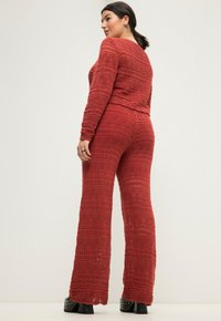 Completo in due pezzi all'uncinetto di un rosso intenso, con un motivo testurizzato a linee ondulate. Top a vestibilità ampia e pantaloni a zampa, abbinati a scarpe con plateau.
