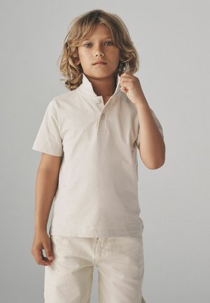 Camisa polo de algodón de color claro con cuello abotonado y mangas cortas, combinada con pantalones de color claro a juego. Diseño sencillo y sólido.