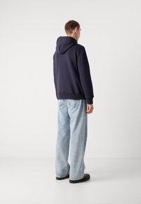 Felpa navy con tasca a marsupio, vestibilità rilassata, abbinata a jeans neri a gamba larga e scarpe nere. Design minimalista, senza pattern visibili.