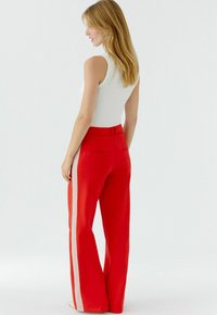 Rode broek met wijde pijpen en crèmekleurige strepen aan de zijkant, met een gladde textuur en achterzakken, gecombineerd met een strak wit tanktopje.