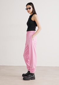 Svart ärmlös topp som matchas med rosa mönstrade vida byxor och svarta kraftiga ankelskors. Byxorna har resårmidja och fickor.