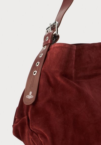 Sac à main en suède rouge profond avec une sangle en cuir marron réglable, dotée de boucles en argent et d'œillets en métal.