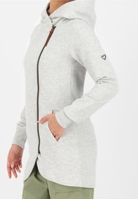 Valkoinen harmaa huppari, jossa on vetoketjukiinnitys, etutaskut ja huppu. Hihan sydänyksityiskohta, valmistettu pehmeästä kankaasta, hieman istuva muotoilu.