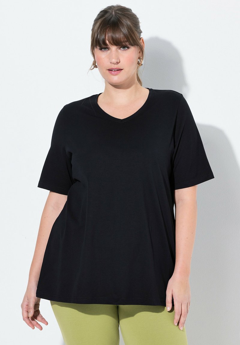 T-shirt nera a maniche corte con scollo a V in morbido tessuto. Vestibilità ampia con orlo dritto. Indossata con leggings verde chiaro.