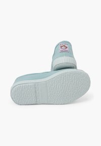 Zapatos de lona azul claro con una suela de goma blanca texturizada, que presentan una etiqueta de marca redonda en el talón y costuras reforzadas en los lados.