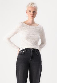 White long-sleeve top with floral lace pattern, round neckline, paired with high-waisted black jeans featuring five pockets and button closure.
