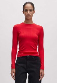 Rotes langärmeliges, geripptes Shirt mit rundem Ausschnitt. Der Stoff scheint dehnbar und eng anliegend zu sein. Kombiniert mit hochtaillierten schwarzen Jeans.