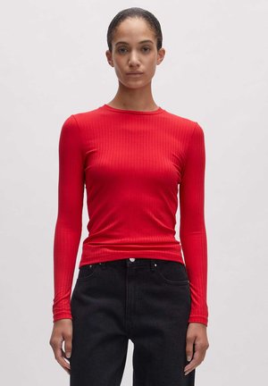 Rode lange mouwen rib shirt met een ronde halslijn. De stof lijkt rekbaar en aansluitend. Draagt met hooggetailleerde zwarte jeans.