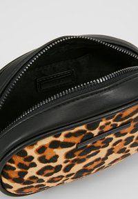 Svart läderväska med leopardtryck på framsidan, rundad form, dragkedjestängning och inredning med foder. Märkesetikett synlig inuti.