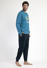 Sudadera color azul verdoso con estampado gráfico, cuello redondo y puños de canalé, combinada con joggers ajustados de color azul oscuro que tienen bolsillos laterales.