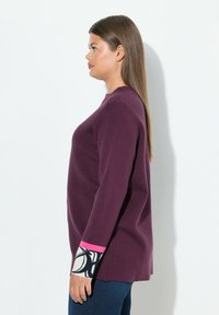 Maglione viola con scollo rotondo, maniche lunghe, polsini a contrasto con motivo in bianco e nero e dettagli rosa. Texture in maglia morbida.