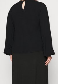 Sort langærmet bluse med en nøglehulslukning bagpå, der har en glat tekstur og flagrende ærmer. Ideel til lagdeling eller afslappet brug.