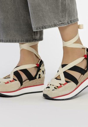 Chaussures à talons compensés beiges avec des sangles noires et des accents rouges. La tige présente un motif léopard et un doux daim. Semelle intermédiaire en corde pour ajouter de la texture.