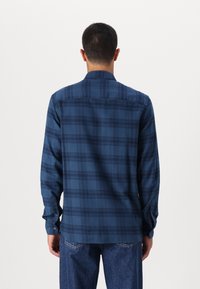 Koszula w kratę z długim rękawem w ciemnym niebieskim kolorze z wzorem w kratkę. Posiada klasyczny kołnierz oraz mankiety zapinane na guziki. Gładka faktura tkaniny.