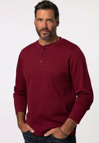 Bordeaux-rotes Langarm-Henley-Shirt mit drei braunen Knöpfen am Kragen. Hergestellt aus geripptem Stoff, mit einem lässigen Schnitt und Rundhalsausschnitt.