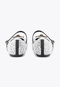 Chaussures noir et blanc avec un dos texturé orné de sequins blancs, une bride et un accent noirs, ainsi qu'une petite décoration dorée à l'avant.