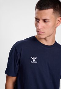 Mørkeblå bomullst-skjorte med korte ermer, med et hvitt brodert "hummel"-logo på venstre side av brystet.